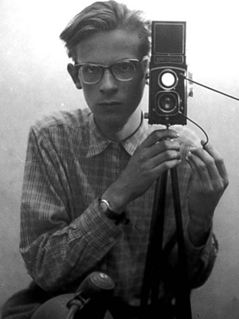 Ein Mann mit Brille und im Hemd hinter einer Kamera auf einem Stativ.