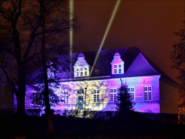 Foto vom Schlossleuchten 2012: Schloss Landestrost leuchtet in blauem Licht, zwei starke Scheinwerfer malen außerdem zwei Lichtsäulen in den Himmel.
