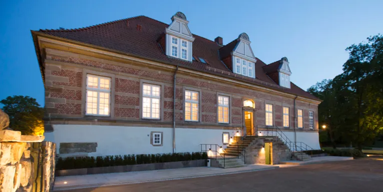 Ein Schloss in der Außenansicht bei Dämmerung. Sowohl drinnen als auch draußen ist die Beleuchtung an.
