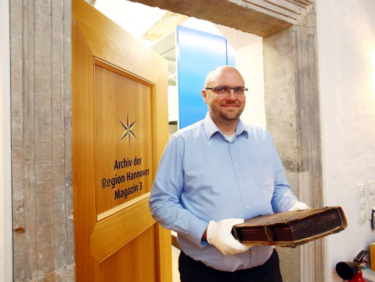 Ein Mann mit weißen Handschuhen an, mit denen er einen Folianten hält.