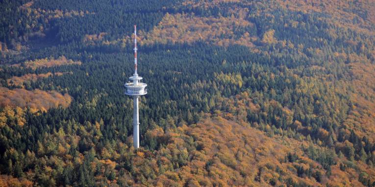 Luftbild eines Höhenzuges mit einem Laub-/Nadelwald im Herbst und einem Funkturm