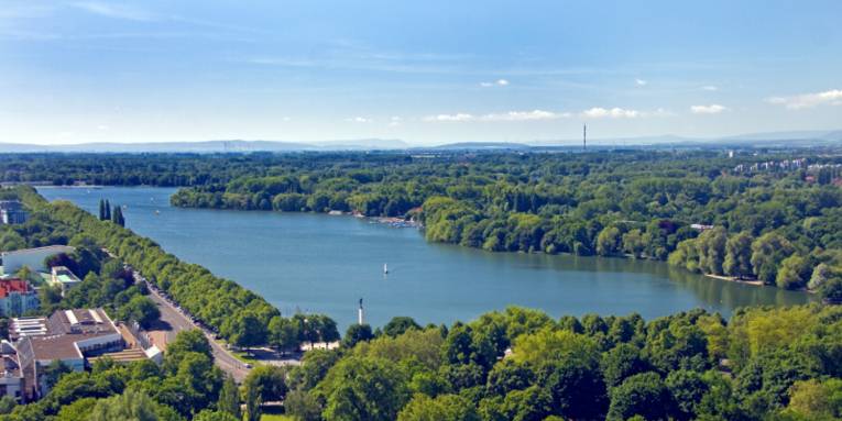 Die Wasserfläche des Maschsees ist von grünen Bäumen umgeben, der Himmel leuchtet blau.