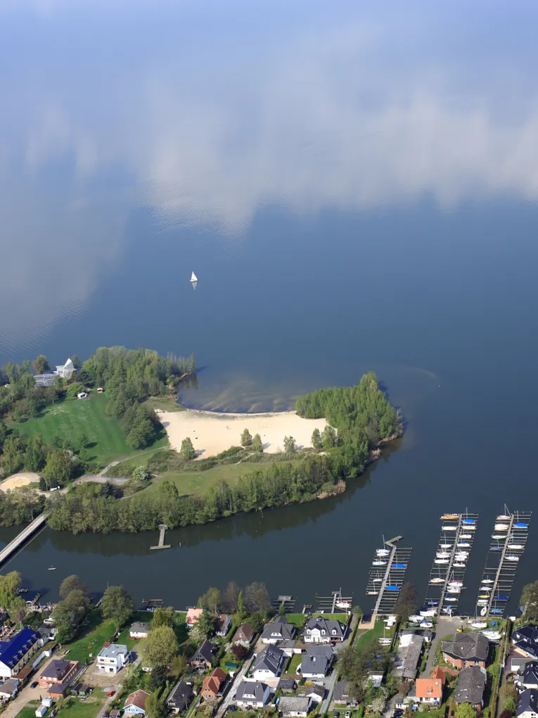 Blick aus einem Flugzeug auf das Ufer des Steinhuder Meeres mit Bootsanlegern und Wald und der Badeinsel.