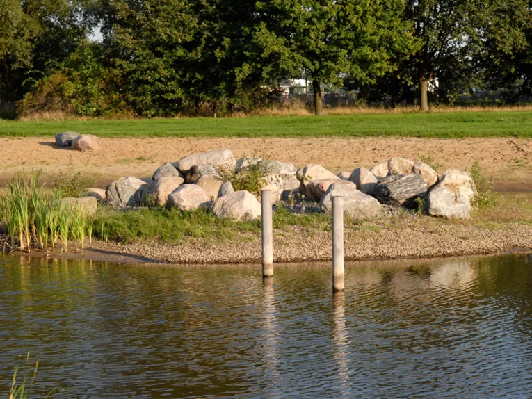 Blick über Wasser auf Feldsteine und Sandstrand