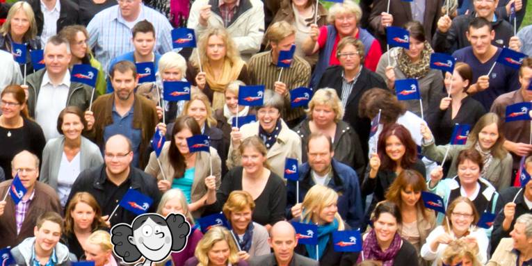 Menschen stehen dicht nebeneinander und halten Fähnchen in ihren Händen, im Vordergrund ist ein gezeichnetes Mädchen über das Foto gelegt.