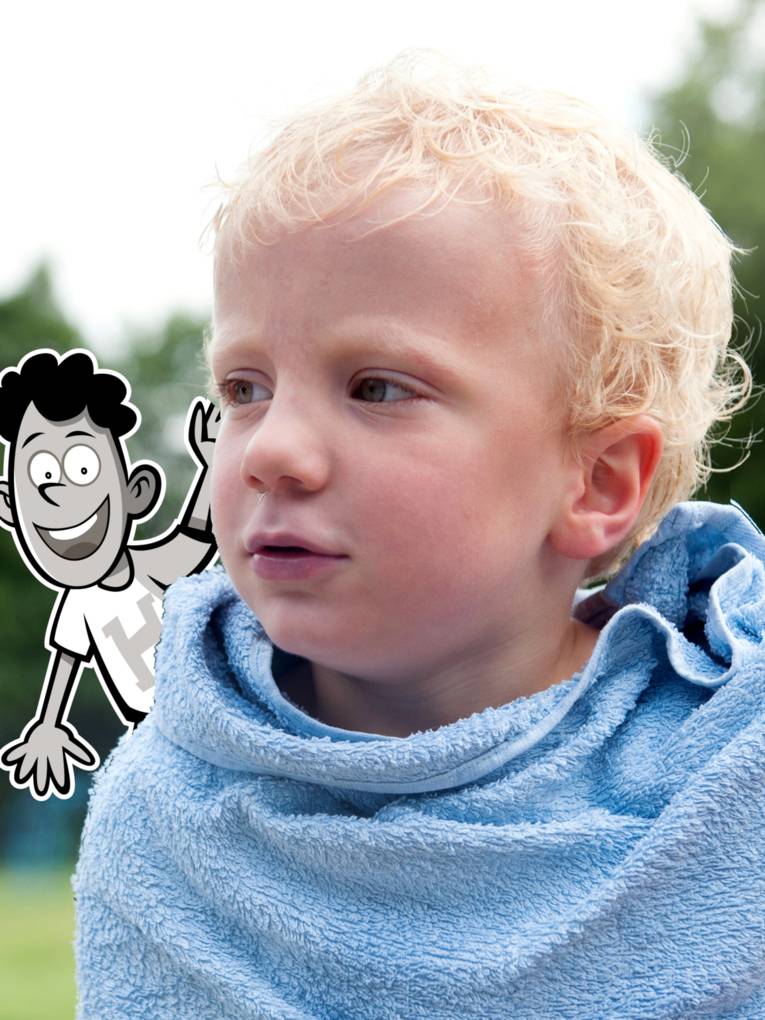 Ein blonder Junge ist in ein blaues Handtuch gewickelt. Im Hintergrund sind grüne Bäume und eine Wiese.