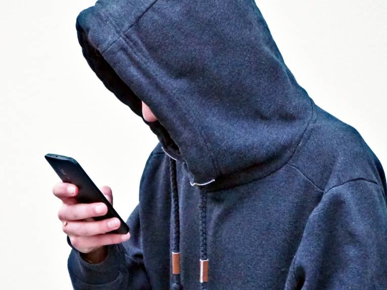 Ein Jugendlicher schaut mit hängenden Schultern in sein Smartphone.