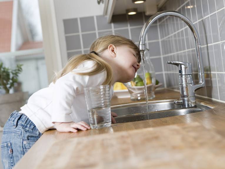 Ein kleines Mädchen in einer Küche trinkt Leitungswasser direkt aus dem Wasserhahn der Spüle