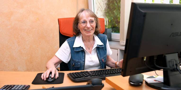 Eine ältere Frau bedient einen PC und lacht.