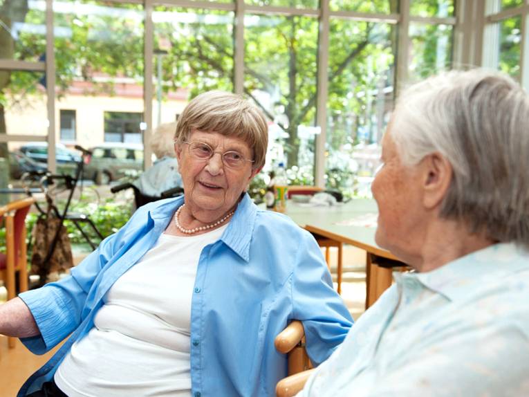 Zwei ältere Damen sitzen auf Stühlen und sprechen miteinander.