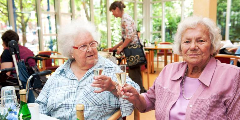 Zwei Seniorinnen stoßen mit einem Getränk an.
