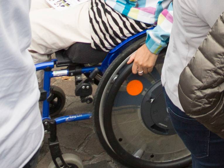 Mehrere Menschen gehen über einen Weg, eine Person fährt in einem Rollstuhl.