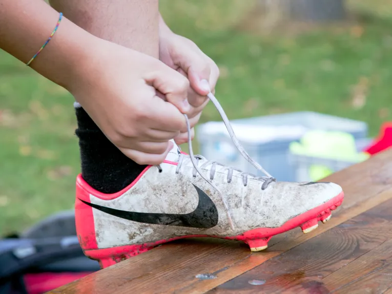 Zwe Hände binden die Schnürsenkel eines Fußballschuhs