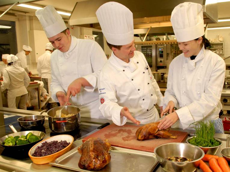 Geflügel, Rotkohl und Brokkoli: zwei Köche und eine Köchin bereiten Speisen zu.