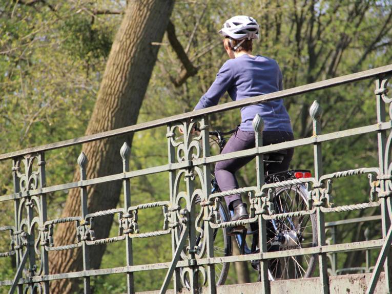 Eine Radfahrerin mit Helm im Frühling auf einer Brücke