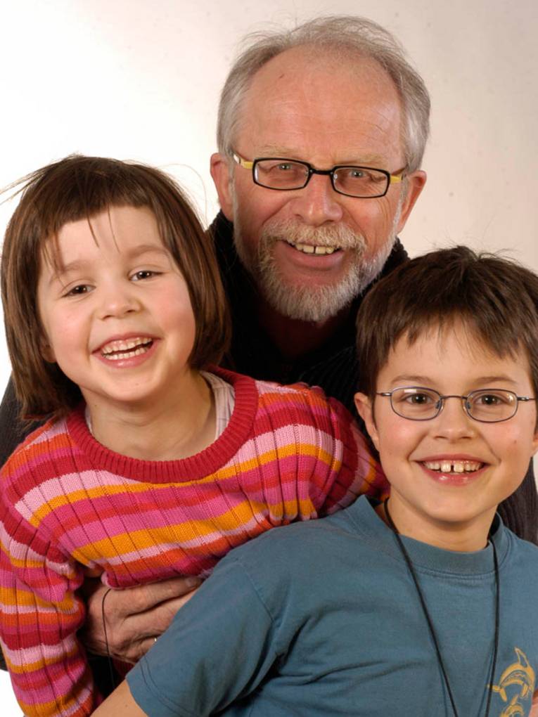 Ein älterer Herr mit Brille, grauem Haar und grauem Vollbart gemeinsam mit einem Mädchen und einem Jungen.