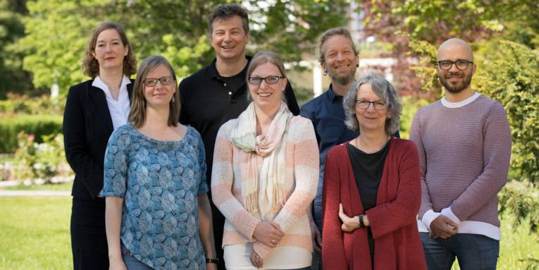 Vier Frauen und drei Männer stehen draußen auf einer Rasenfläche in zwei Reihen.