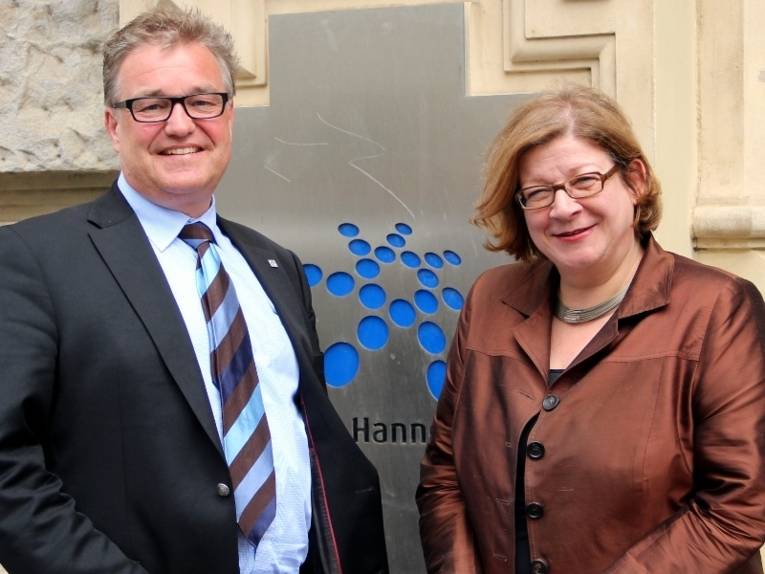 Hauke Jagau und Andrea Fischer stehen vor dem Regionshaus. Das Logo der Region Hannover ist zwischen ihnen zu erkennen. 