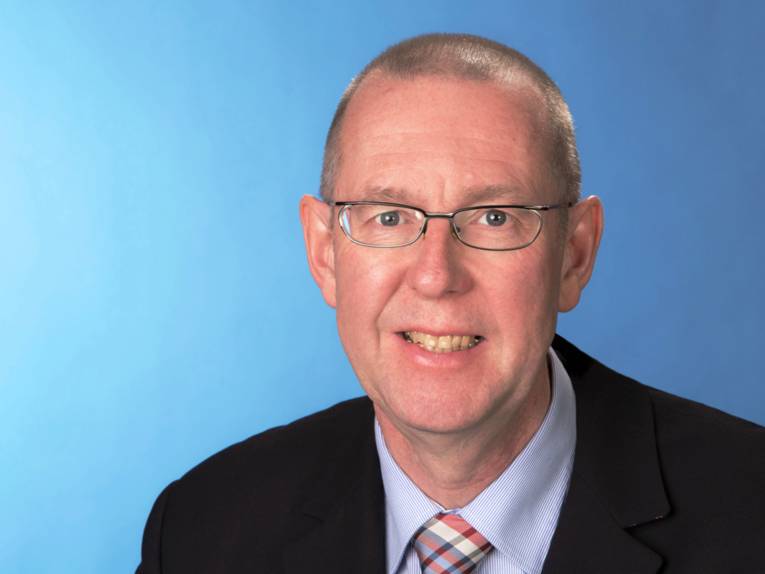 Portraitfoto von Prof. Dr. Axel Priebs vor blauem Hintergrund