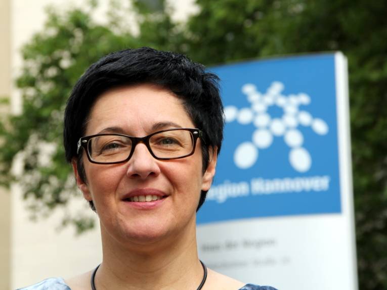 Porträt einer Frau mit Brille und kurzen, dunklen Haaren vor dem Logo der Region Hannover.