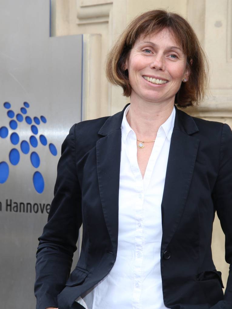 Sylvia Thiel, Beauftragte für Menschen mit Behinderungen der Region Hannover, steht vor einem Eingang zum Regionshaus, hinter ihr ist das Logo der Region Hannover.