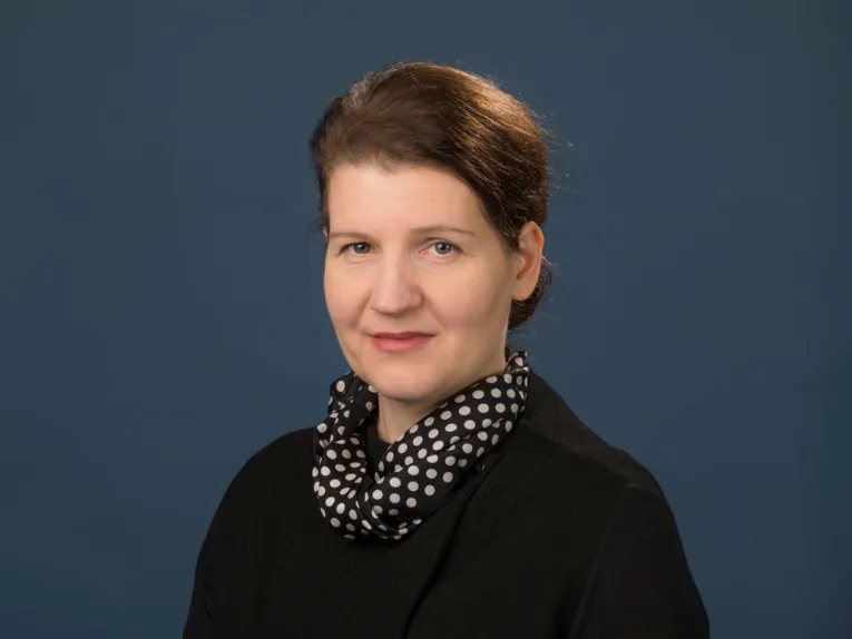 Portraitaufnahme einer Frau mit dunklem Oberteil und einem gepunktetem Halstuch.