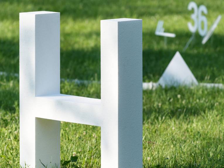 Ein weißes H steht mit weiteren Symbolen einer Wetterkarte auf einer Rasenfläche. Zusammen bilden sie die begehbare Wetterkarte des 5. Juli 2015 – dem bislang heißesten Tag in Deutschland seit Beginn der Wetteraufzeichnungen.