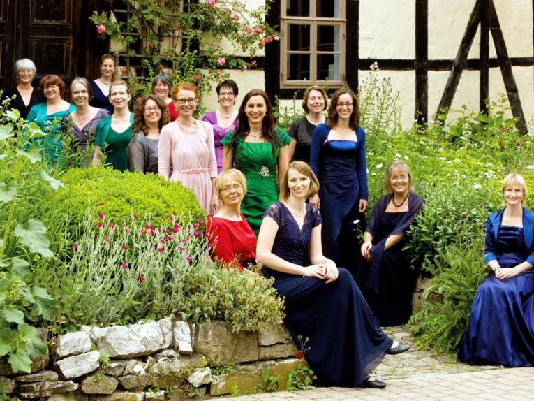 Frauen tragen Abendkleider und stehen oder sitzen in einem Garten.