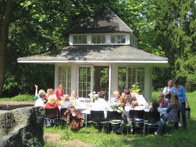 Menschen sitzen an einer gedeckten Tafel vor dem Teepavillon des Hermannshofs in Springe-Völksen.