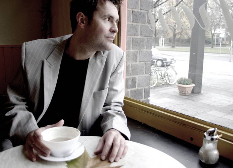 Ein Mann trinkt einen Kaffee und schaut aus einem Fenster.