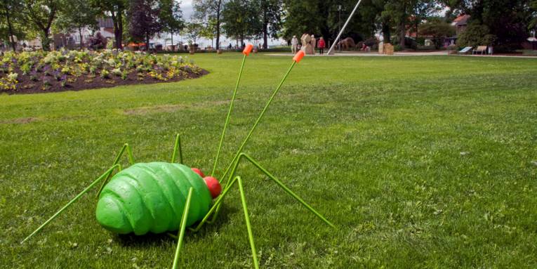 Eine Skulptur in Form einer großen Blattlaus steht auf einer Rasenfläche eines Parks.