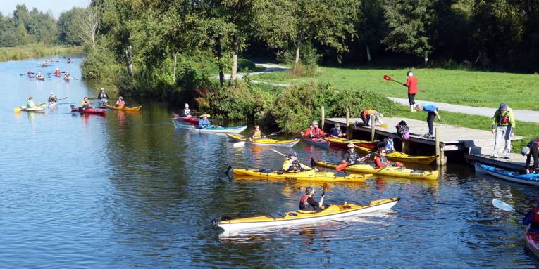 Menschen fahren mit Kanus im Hagenburger Kanal, ihr Ziel scheint eine Anlegestelle zu sein.