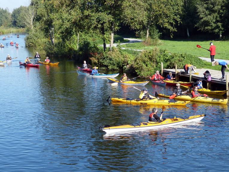 Menschen fahren mit Kanus im Hagenburger Kanal, ihr Ziel scheint eine Anlegestelle zu sein.