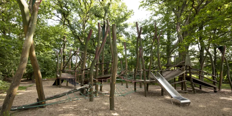 Abenteuerspielplatz mit Rutsche in mitten von Laubbäumen