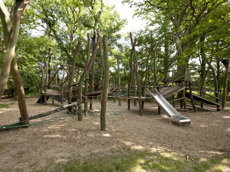 Abenteuerspielplatz mit Rutsche in mitten von Laubbäumen