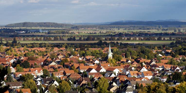 Vorne geht der Blick über die Dächer der Stadt Springe, dahinter zeichnet sich eine Landschaft mit Wald, Wiesen, Windrädern und Erhebungen des Deisters ab.