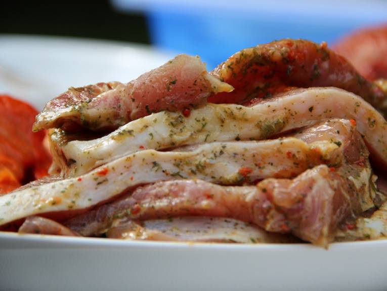 Mehrere Fleischscheiben, die noch ungegrillt sind und auf einem Teller liegen.