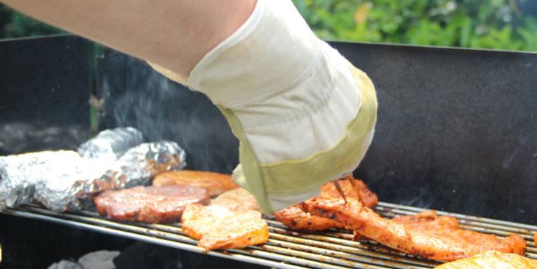 Hand in Handschuh, Grillgut, das gerade gewendet wird