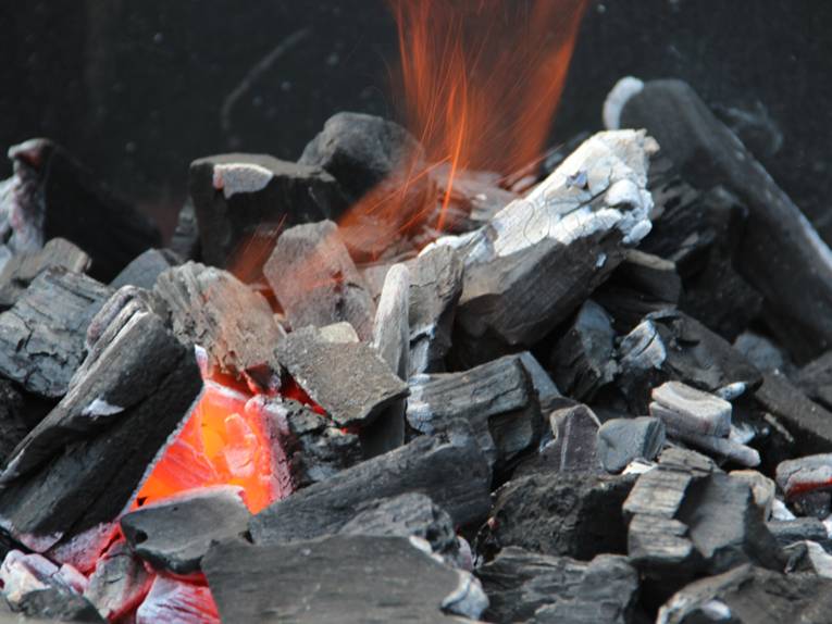 Grillkohle, die bereits entzündet ist. Es sind Glut und auch eine kleine Flamme zu sehen.