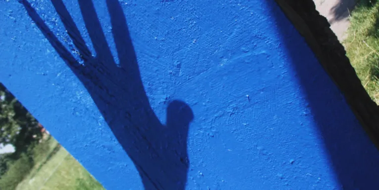 Schatten einer Hand auf einem leuchtend blauen Betonpfahl