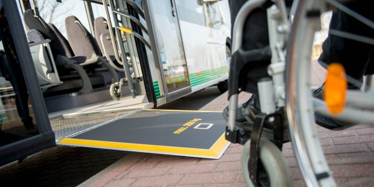 Ein Rollstuhlfahren, der sich auf die Rampe eines Linienbusses zubewegt.