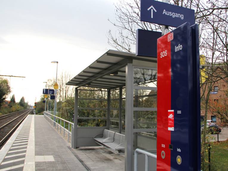Blick auf den Bahnsteig des S-Bahnhofs Empelde. Links verlaufen die Schienen, rechts steht ein Wetterschutzhäuschen mit Notruf- und Infosäule.