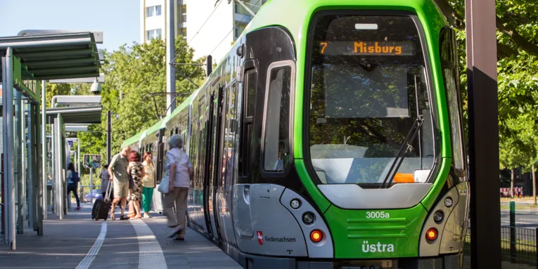 Ein TW3000 hält an einem Hochbahnsteig der Linie 7 in Richtung Misburg, die Stadtbahn lässt Fahrgäste an der Haltestelle ein- und aussteigen.