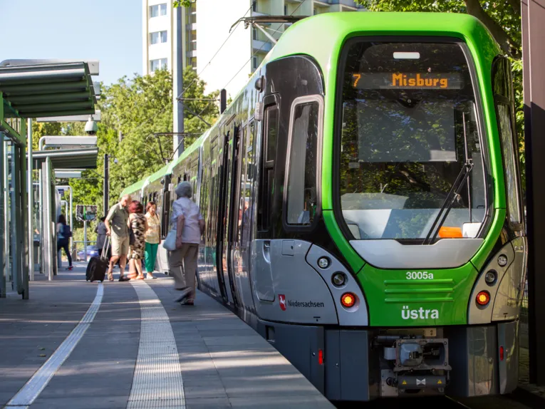 Ein TW3000 hält an einem Hochbahnsteig der Linie 7 in Richtung Misburg, die Stadtbahn lässt Fahrgäste an der Haltestelle ein- und aussteigen.