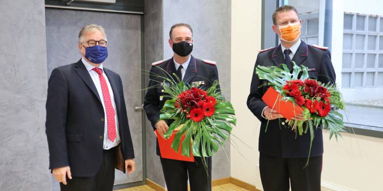 Drei Männer stehen nebeneinander, sie halten Abstand und tragen Mund- Nasen-Bedeckungen. Die zwei Männer neben Regionspräsident Hauke Jagau tragen den Dienstanzug der Freiwilligen Feuerwehr.