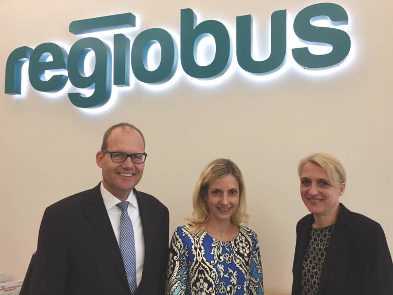 Ein Mann und zwei Frauen stehen nebeneinander, im Hintergrund ist der leuchtende Schriftzug "regiobus".