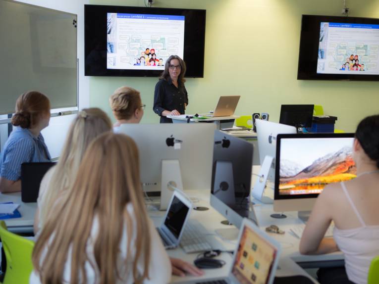 Eine Lehrerin und Schülerinnen in einem Multimedia-Raum.