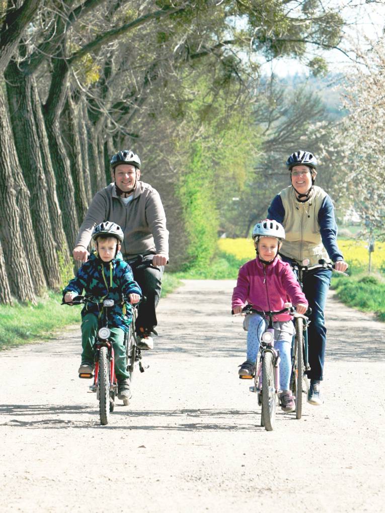 Eine Familie ist auf Fahrrädern unterwegs, die Kinder fahren vorweg, die Erwachsenen hinterher.