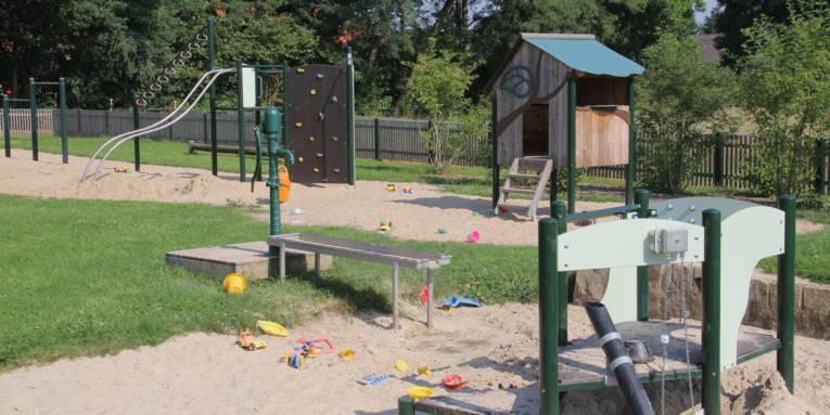Rutschenturm mit Kletterwand, Wasserpumpe und weitere Spielgeräte auf einem Kinderspielplatz.