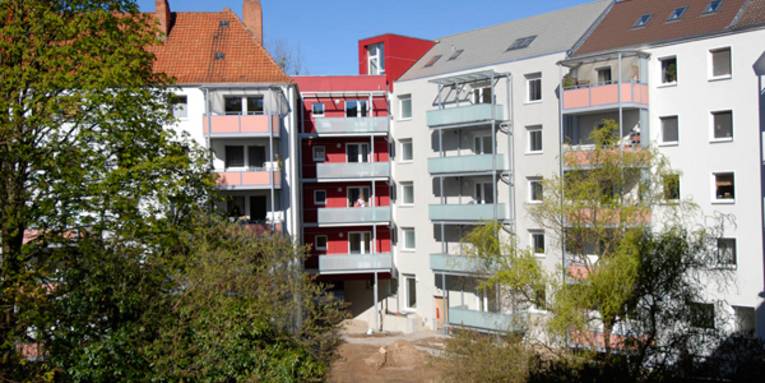 Mehrgeschossige weisse Wohnhäuser mit farbigen Balkons, im Vordergrund Bäume